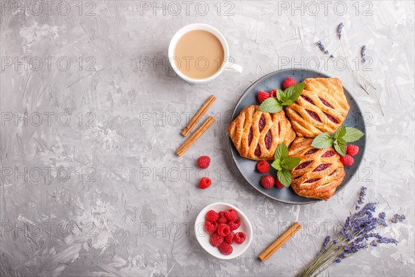 Puff pastry buns with strawberry jam on blue ceramic plate on gray concrete background, cup of