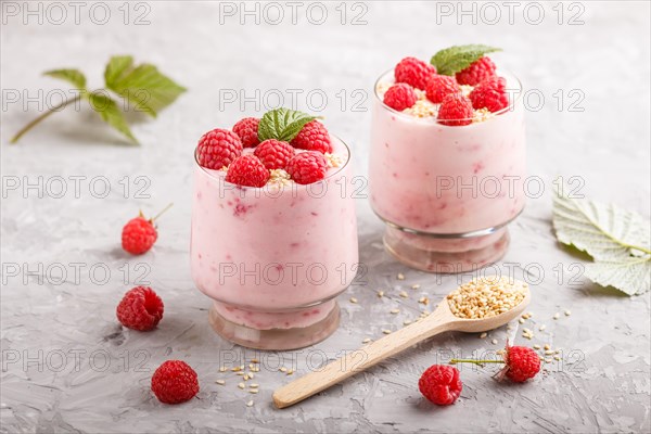 Yoghurt with raspberry and sesame in a glass and wooden spoon on gray concrete background. side