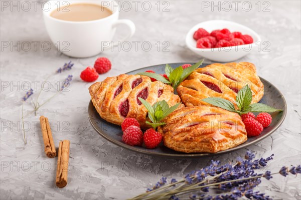 Puff pastry buns with strawberry jam on blue ceramic plate on gray concrete background, cup of