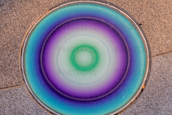Closeup round glass of blue, green and purple inlaid in concrete sidewalk in public park in South