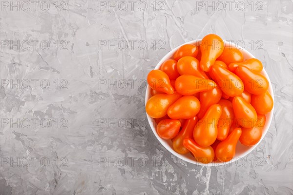 Fresh orange grape tomatoes in white ceramic bowl on gray concrete background. top view, flat lay,