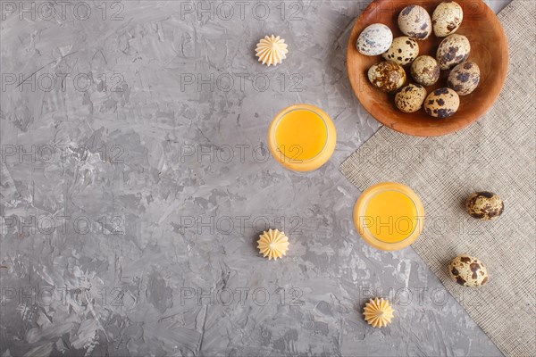 Sweet egg liqueur in glass with quail eggs and meringues on a gray concrete background. Top view,