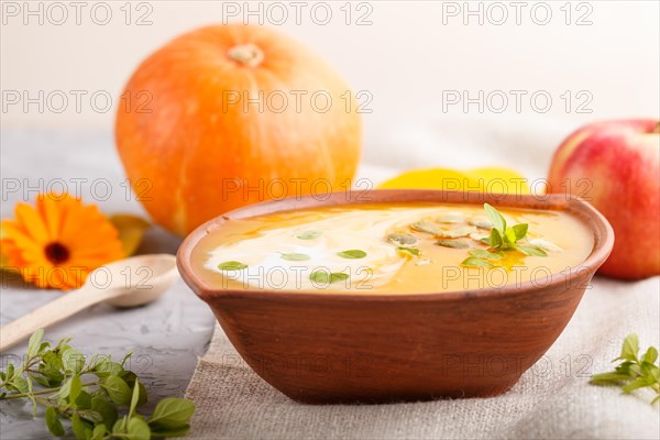 Traditional pumpkin cream soup with seeds in clay bowl on a gray concrete background with linen