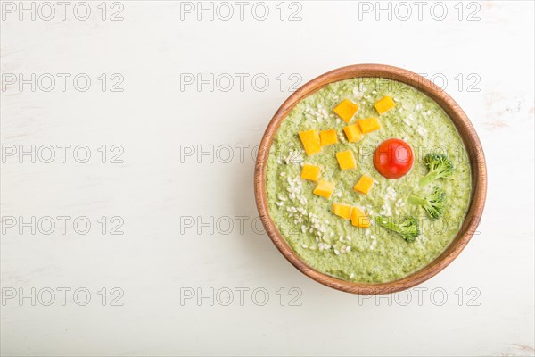 Green broccoli cream soup in wooden bowl on a white wooden background. top view, flat lay, copy
