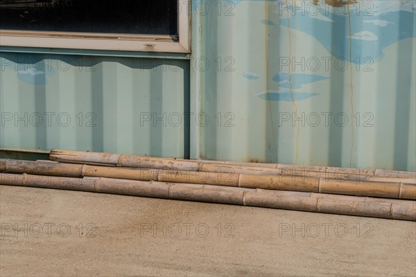 Weathered cracked bamboo poles laying on concrete driveway in front of aluminum building wall in