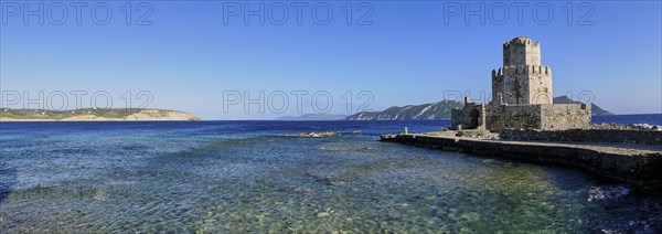 An old stone tower on a coast with crystal clear sea water under a wide blue sky, octagonal