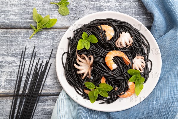 Black cuttlefish ink pasta with shrimps or prawns and small octopuses on gray wooden background and