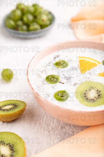 Yogurt with kiwi, gooseberry, chia in ceramic bowl on gray concrete background and orange linen