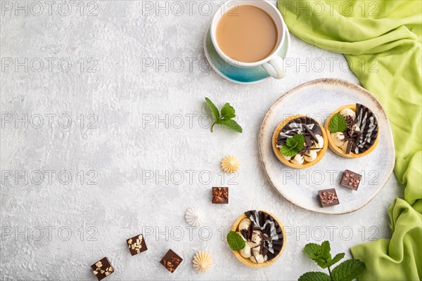 Sweet tartlets with chocolate and cheese cream with cup of coffee on a gray concrete background and