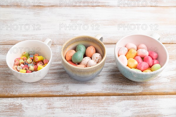 Heap of multicolored caramel candies in cups on white wooden background. copy space, side view,