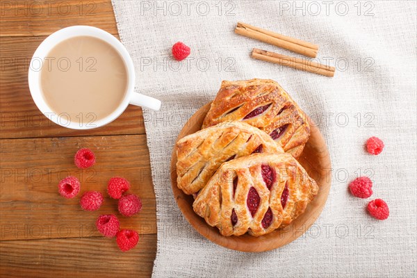 Puff pastry buns with strawberry jam on wooden background with linen textile and a cup of coffee.