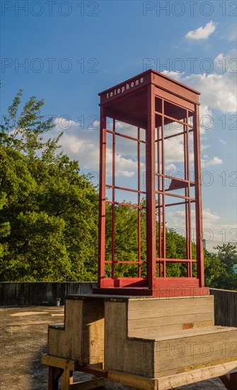 Red wooden telephone booth minus phone and without glass on roof of building on sunny day with blue