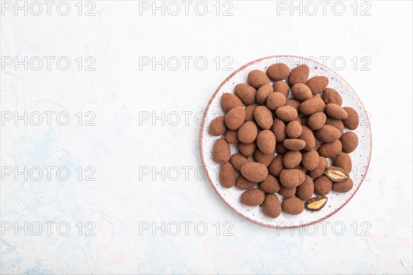 Almond in chocolate dragees on ceramic plate on white concrete background. Top view, copy space,