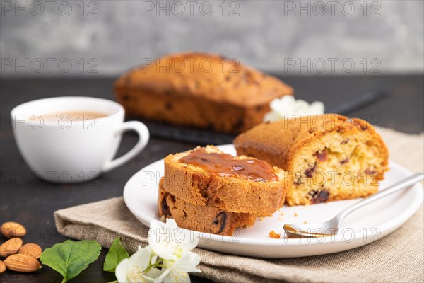 Homemade cake with raisins, almonds, soft caramel and a cup of coffee on a black concrete