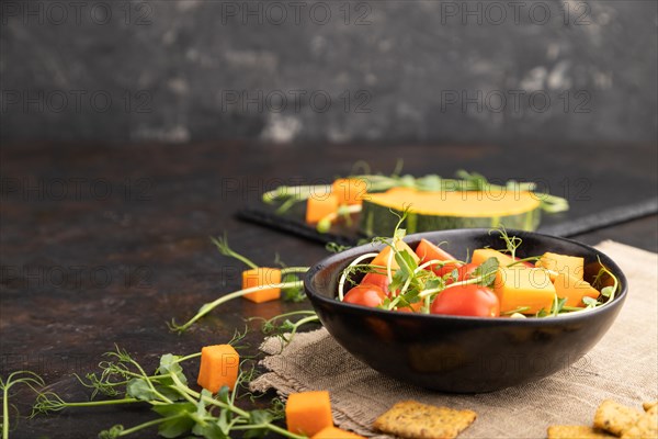 Vegetarian vegetable salad of tomatoes, pumpkin, microgreen pea sprouts on black concrete