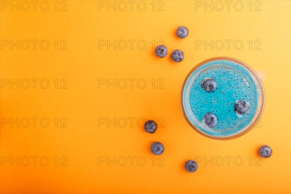 Glass of blueberry blue colored drink with basil seeds on orange background. Morninig, spring,