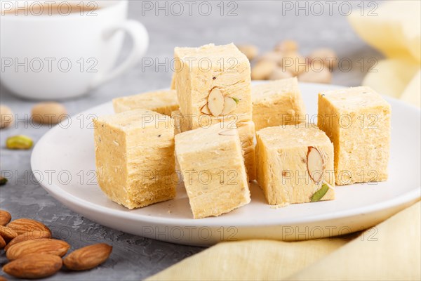 Traditional indian candy soan papdi in white plate with almond, pistache and a cup of coffee on a