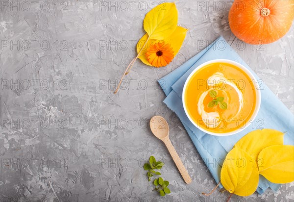 Traditional pumpkin cream soup with in white bowl on a gray concrete background with blue napkin.