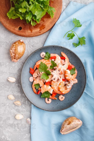 Boiled shrimps or prawns and small octopuses with herbs on a blue ceramic plate on a gray concrete