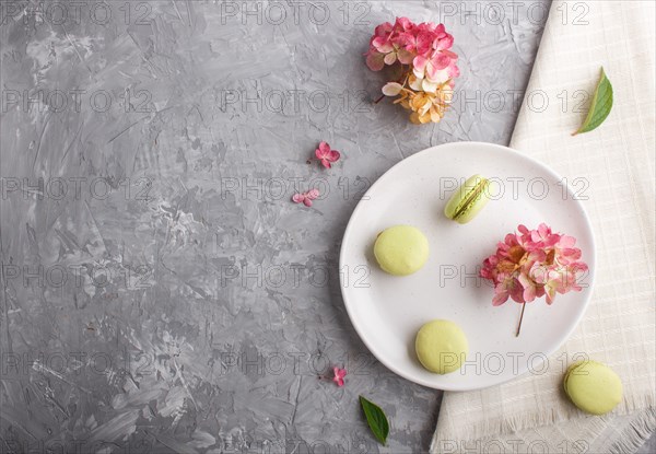 Green macarons or macaroons cakes on white ceramic plate on a gray concrete background and linen
