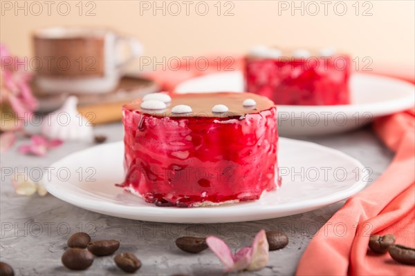 Red cake with souffle cream with cup of coffee on a gray concrete background and red textile. side