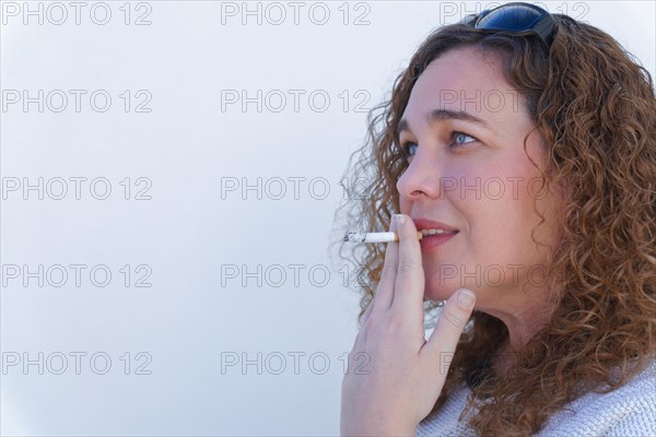 Attractive blue-eyed, curly-haired woman in profile smoking a cigarette with white background and