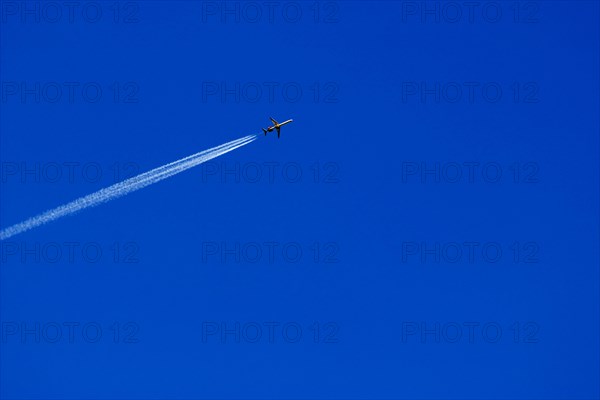 A passenger plane with vapour trail high in the blue sky