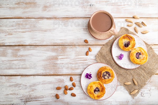 Small cheesecakes with jam and almonds with cup of coffee on a white wooden background and linen