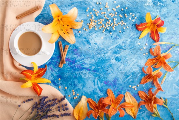 Orange day-lily and lavender flowers and a cup of coffee on a blue concrete background, with orange