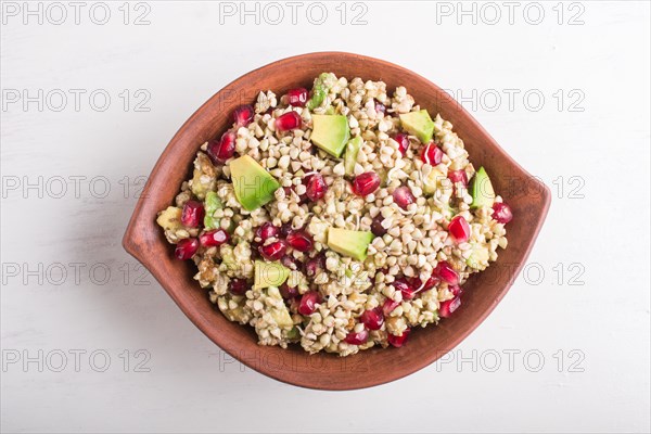 Salad of germinated buckwheat, avocado, walnut and pomegranate seeds in clay plate on white wooden