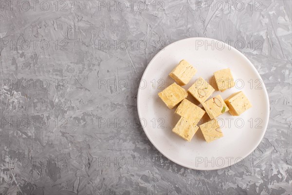 Traditional indian candy soan papdi in white plate with almond and pistache on a gray concrete