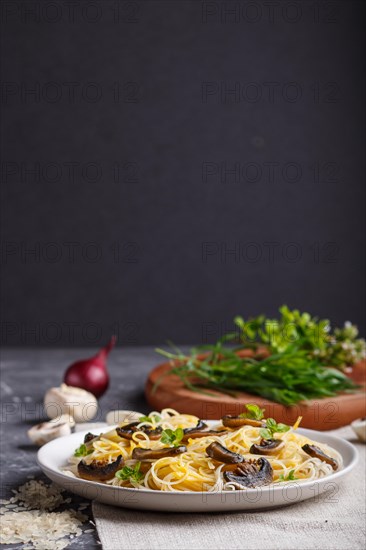 Rice noodles with champignons mushrooms, egg sauce and oregano on white ceramic plate on a black