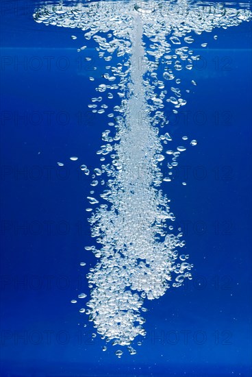 A thin jet of water penetrates the water surface and produces many air bubbles in the blue water of