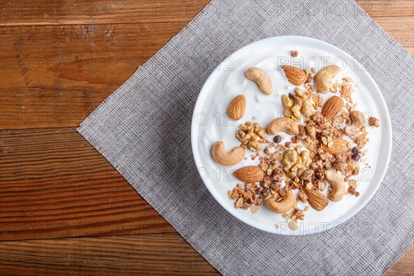 White plate with greek yogurt, granola, almond, cashew, walnuts on brown wooden background. top