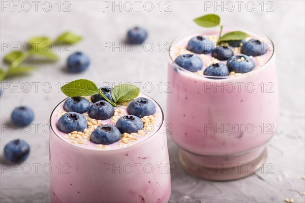 Yoghurt with blueberry and sesame in a glass and wooden spoon on gray concrete background. side