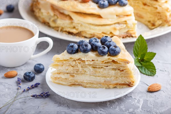 Homemade layered Napoleon cake with milk cream. Decorated with blueberry, almonds, walnuts,