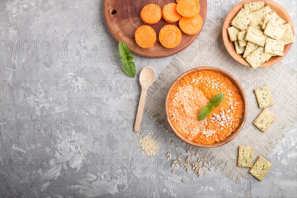 Carrot cream soup with sesame seeds and snacks in wooden bowl on a gray concrete background with