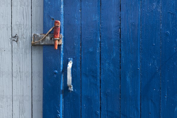 Blue sliding door with handle and red wooden splint to close the wooden wall of a fisherman's hut,