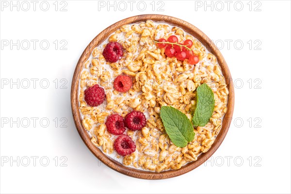 Wheat flakes porridge with milk, raspberry and currant in wooden bowl isolated on white background.