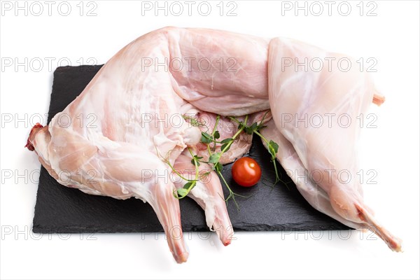 Whole raw rabbit with tomatoes, pea sprouts on a black concrete slate board isolated on white