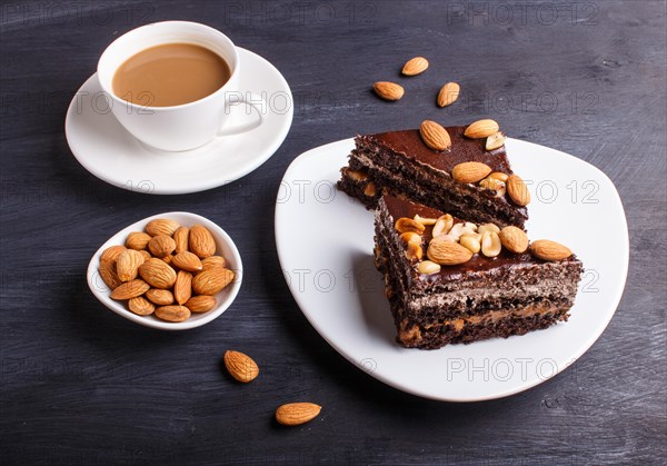 Chocolate cake with caramel, peanuts and almonds on a black wooden background. cup of coffee, close