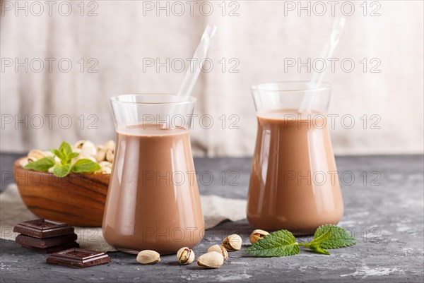 Organic non dairy pistache chocolate milk in glass and wooden plate with pistache nuts on a gray