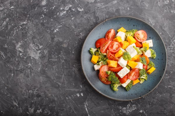 Vegetarian salad with broccoli, tomatoes, feta cheese, and pumpkin on a blue ceramic plate on a