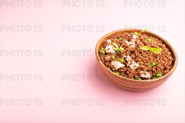 Quinoa porridge with green pea and chicken in wooden bowl on a pastel pink background. Side view,