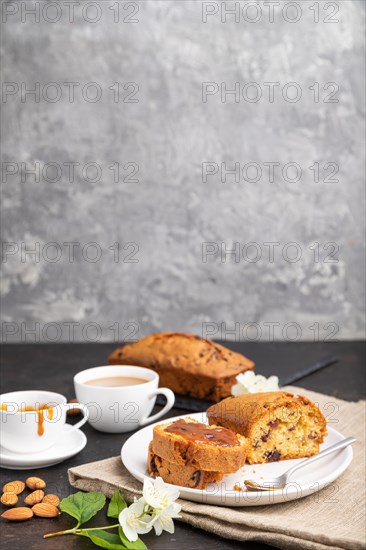 Homemade cake with raisins, almonds, soft caramel and a cup of coffee on a black concrete