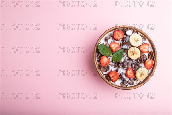 Chocolate cornflakes with milk and strawberry in wooden bowl on pink pastel background. Top view,