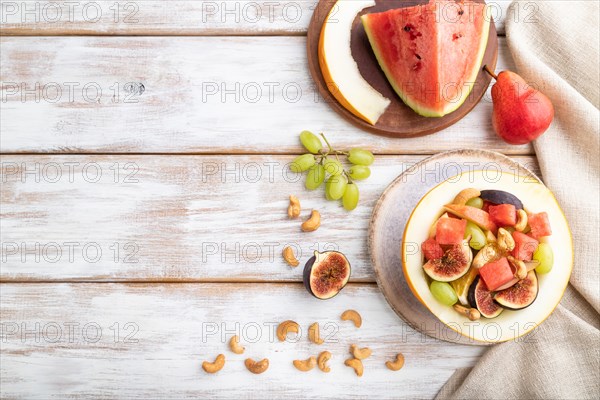 Vegetarian fruit salad of watermelon, grapes, figs, pear, orange, cashew on white wooden background