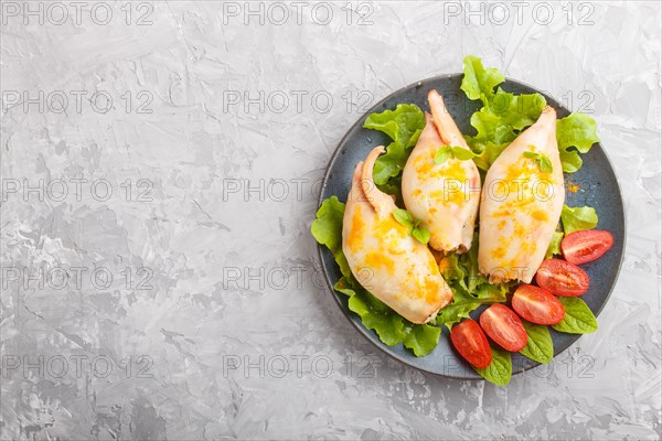 Stuffed baked squid with greens on a blue ceramic plate on a gray concrete background, top view,