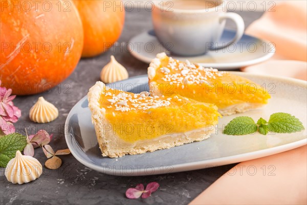 Two pieces of traditional american pumpkin pie with cup of coffee on a black concrete background