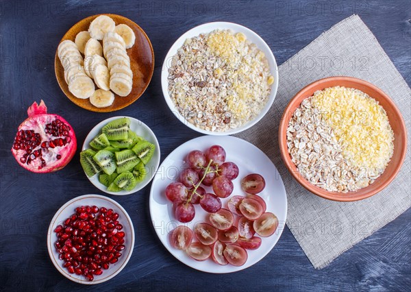 A set of plates with muesli, grapes, kiwi, pomegranate, banana on a black wooden background. top